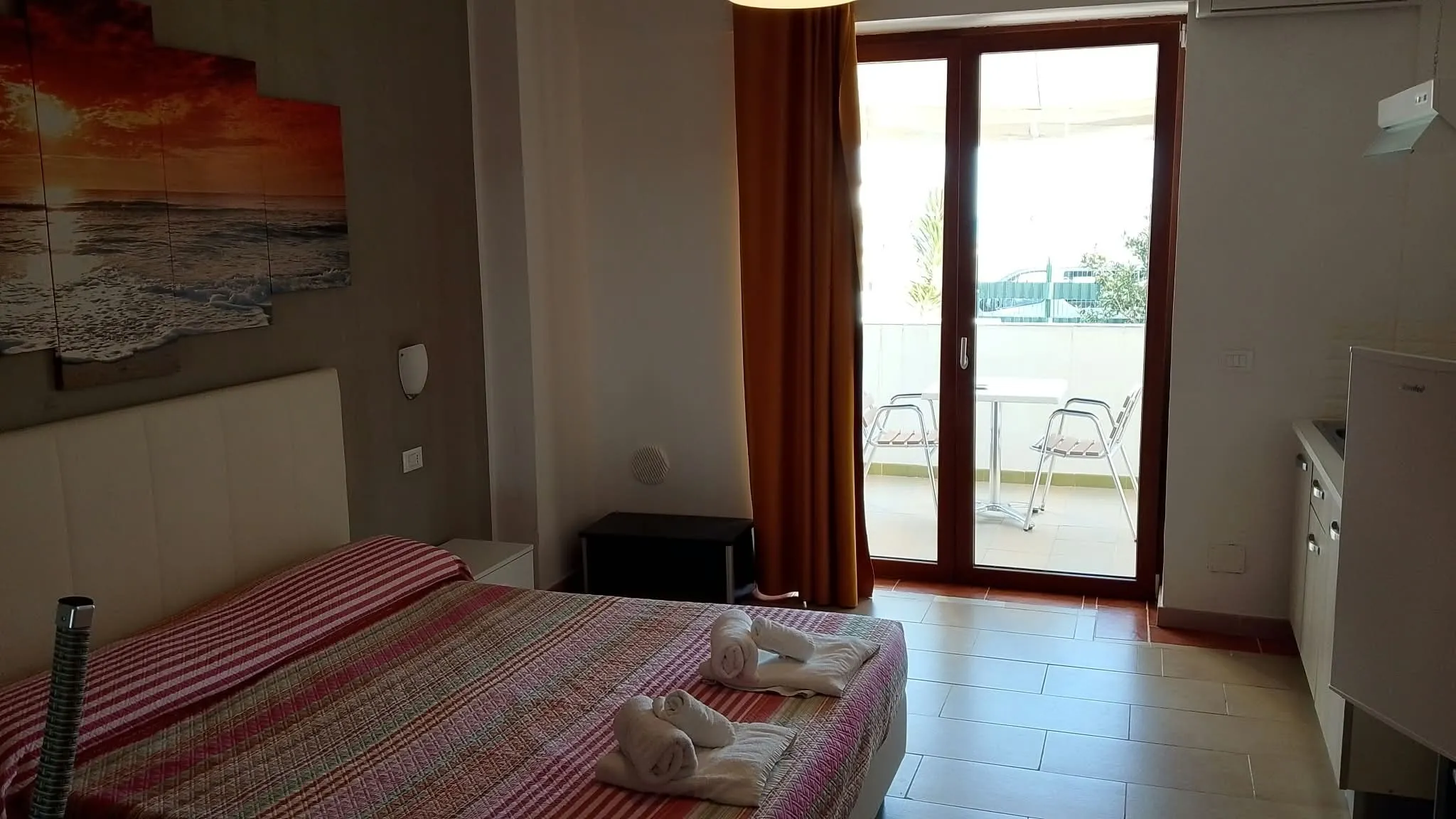 Appartamento 2a: il letto, l’angolo cottura e la porta finestra sulla veranda