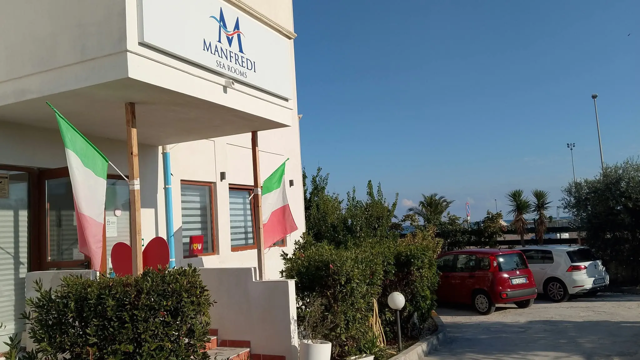 L’ingresso con l’insegna e le bandiere; a destra il parcheggio
