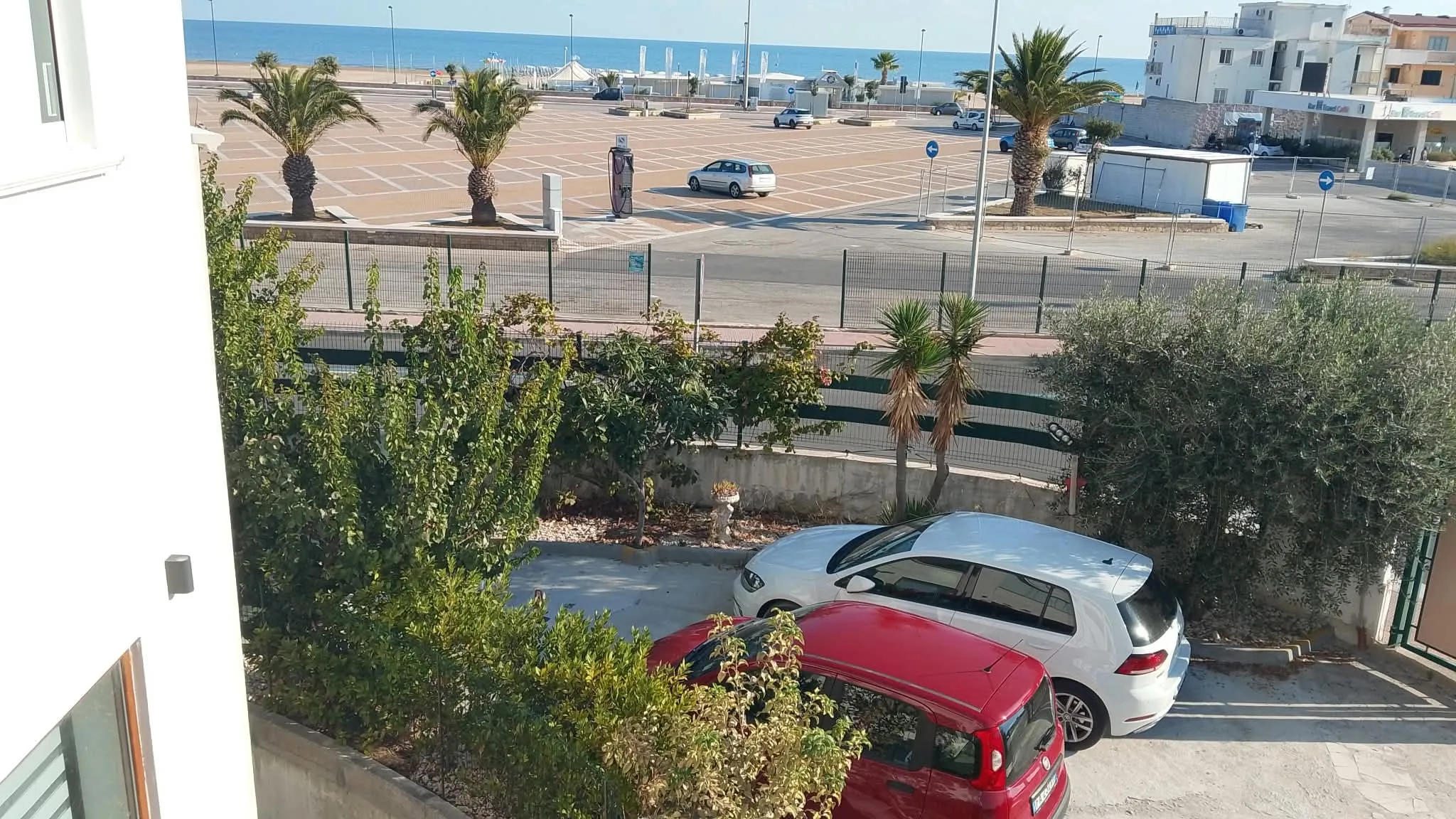 Dalla veranda: il piazzale con le palme e il mare all’orizzonte; sotto, il parcheggio